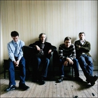 Bandfoto Teenage Fanclub, in ienem leeren Zimmer auf eienem Sofa sitzend